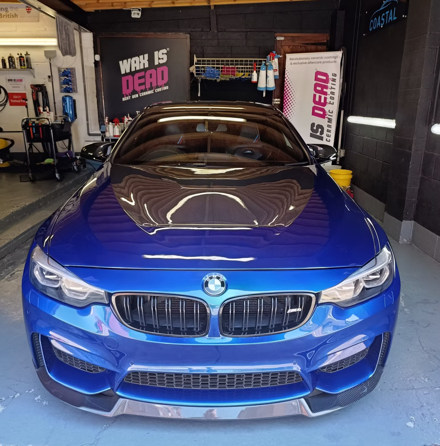 Blue BMW M4 inside the Coastal Car Care detailing studio with Wax is Dead branding